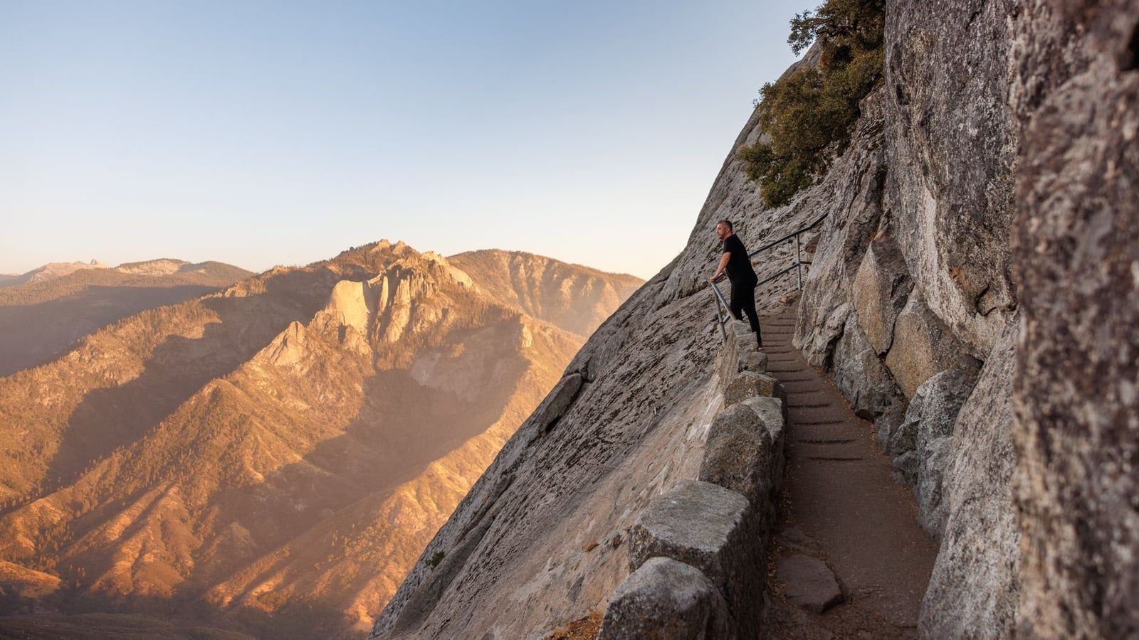 Un excursionista se encuentra en la escalera de piedra construida sobre el empinado acantilado de granito de Moro Rock en el Parque Nacional Sequoia al atardecer.