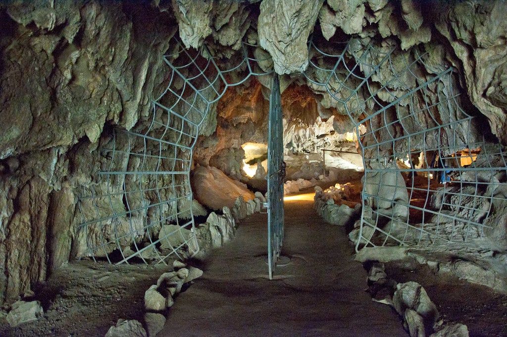 An ornate spider-web metal gate stands open along the walking path inside Crystal Cave in Sequoia National Park.